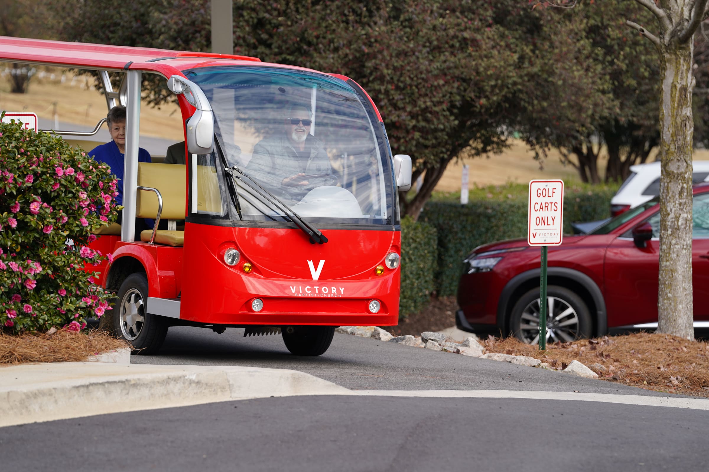 Victory's red golf cart pulling up in the parking lot with a driver and a guest aboard